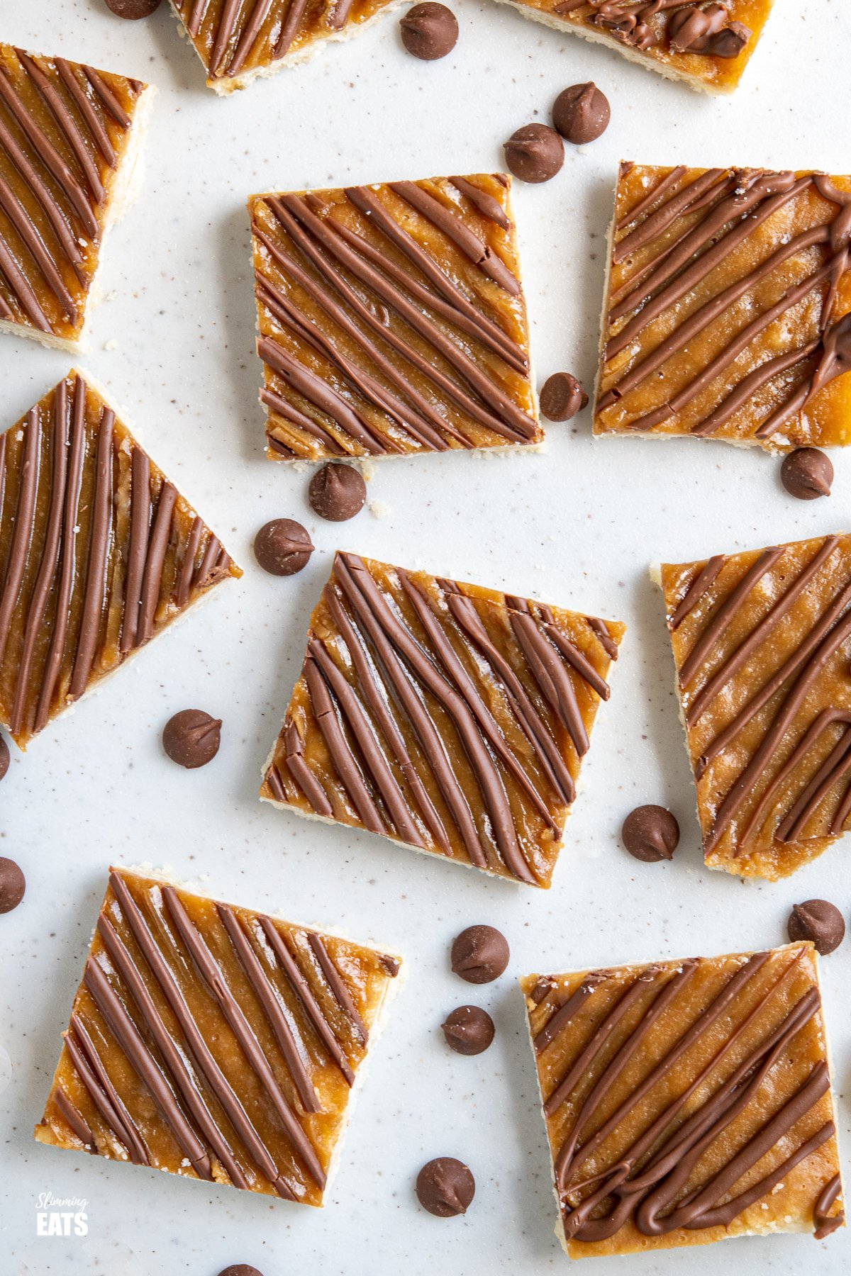 sliced  Millionaires Shortbread Squares on a white board with scattered chocolate chips