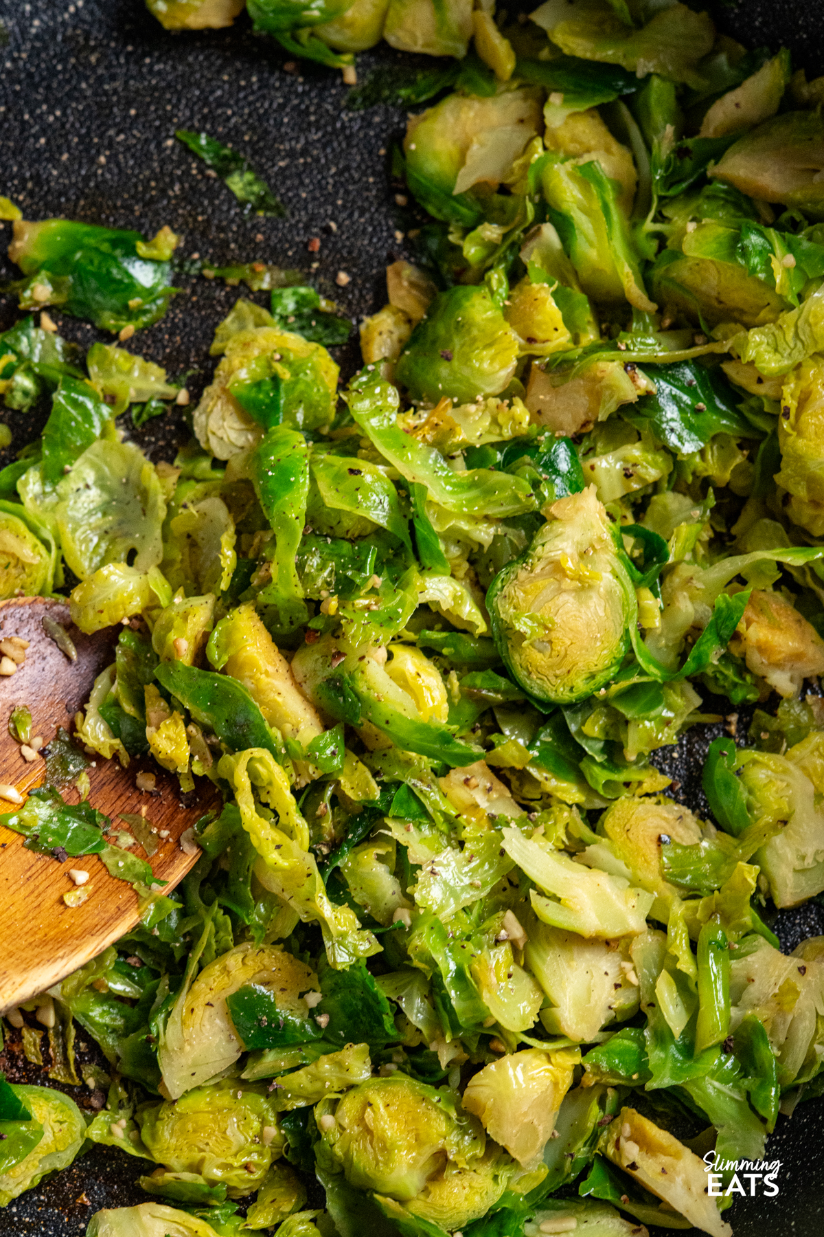 close up of Sauteed Shredded Garlic Brussel Sprouts in non stick frying pan with wooden spoon