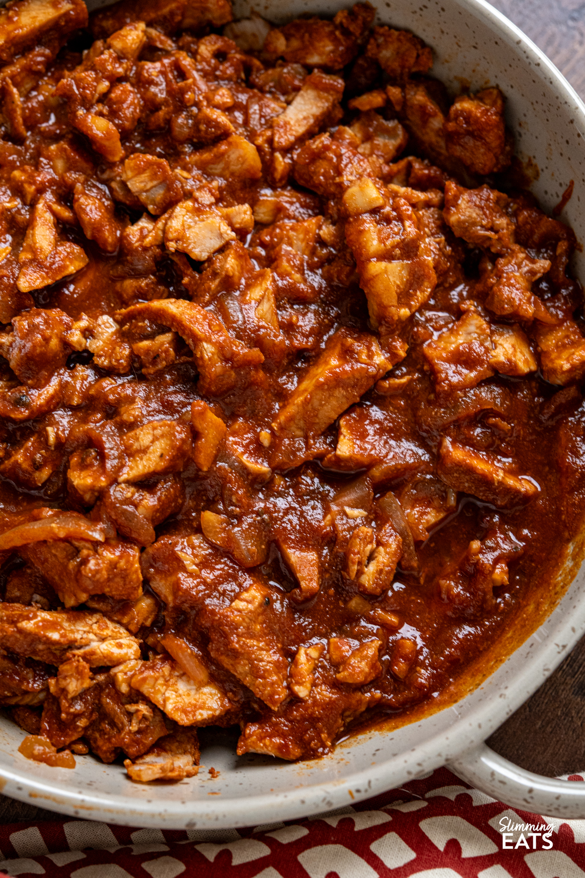 close up of stove top spicy bbq pork in a double handled brown grey ceramic dish 