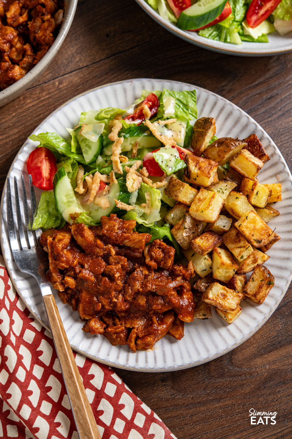 servingof stove top spicy bbq pork on white plate with mixed salad and garlic and herb roast potatoes 