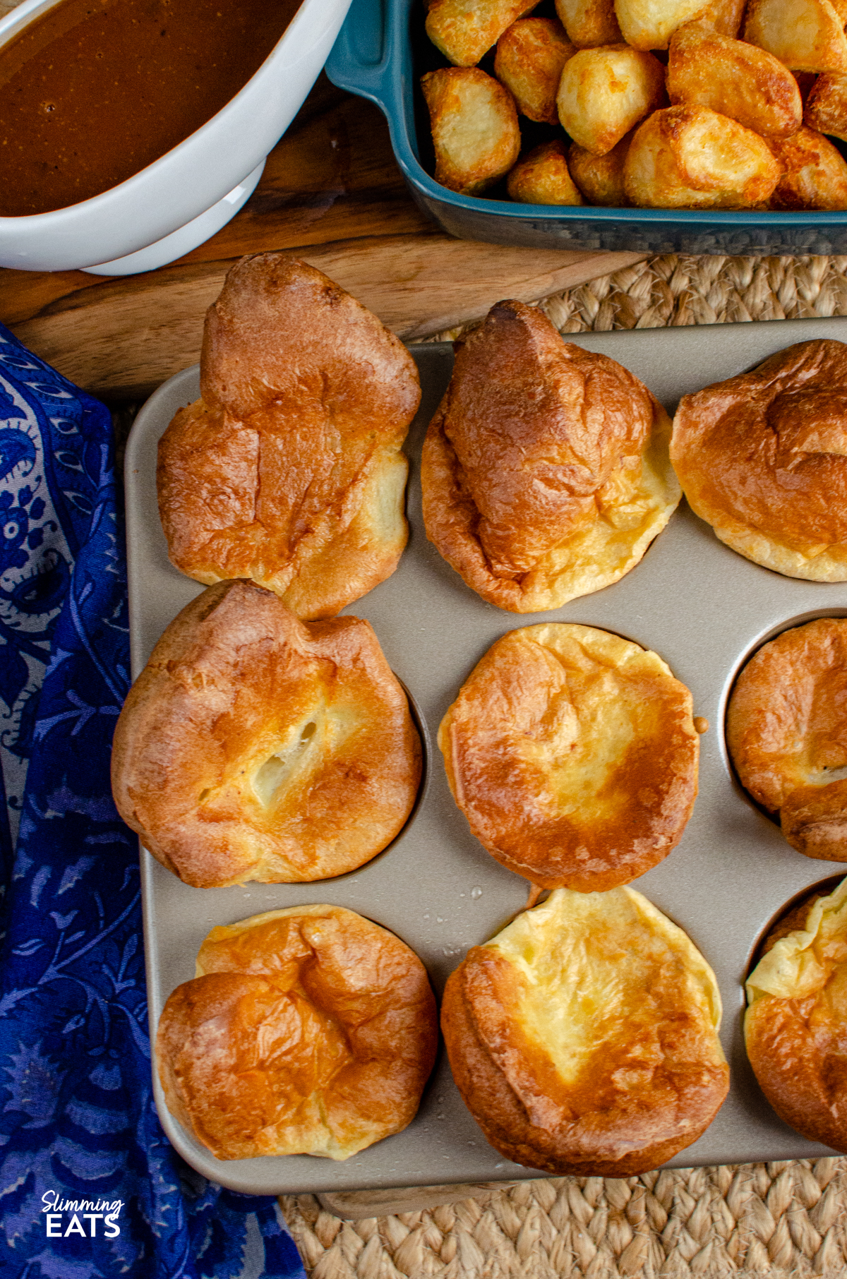 yorkshire puddings cooked in a muffin tray with a jug of gravy and dish with roast potatoes.