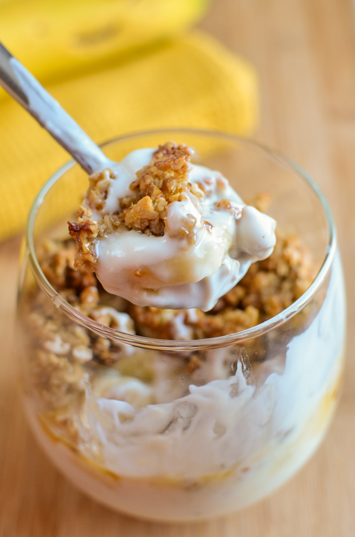 Banana Granola Parfaits - creamy yoghurt layered with homemade banana granola and fresh banana for an easy breakfast or sweet treat. The crunchy granola combined with the creamy yoghurt makes every spoonful so delicious and perfect any time of day. spoon scooping up Banana Granola Yoghurt Parfait from a glass.