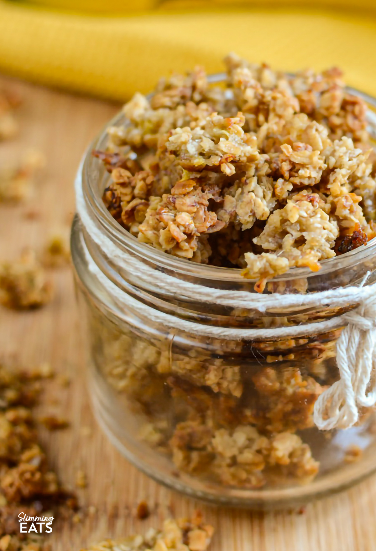 Banana granola beautifully presented in a small jar, decorated with a white rope thread tied around it, and whole bananas in the background for a natural, appetizing setting
