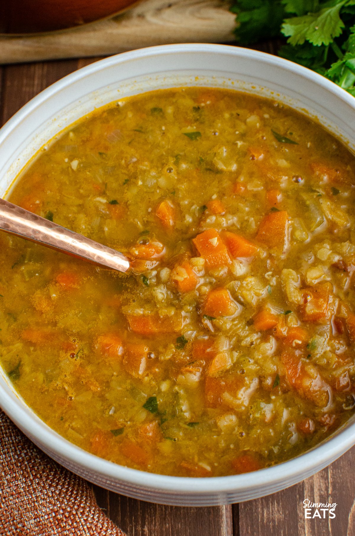 Spicy carrot and lentil soup served in a white bowl with a spoon