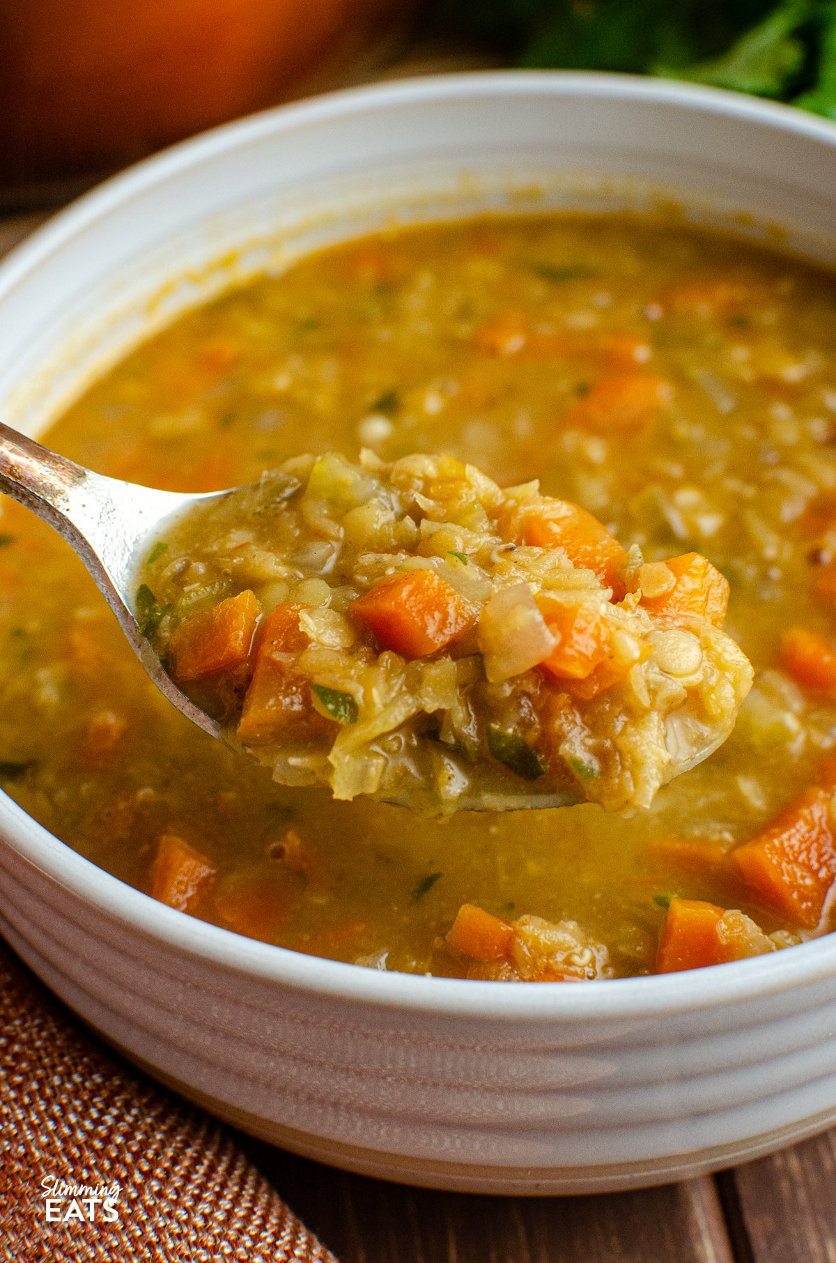 Spoon scooping up a serving of spicy carrot and lentil soup from a bowl.