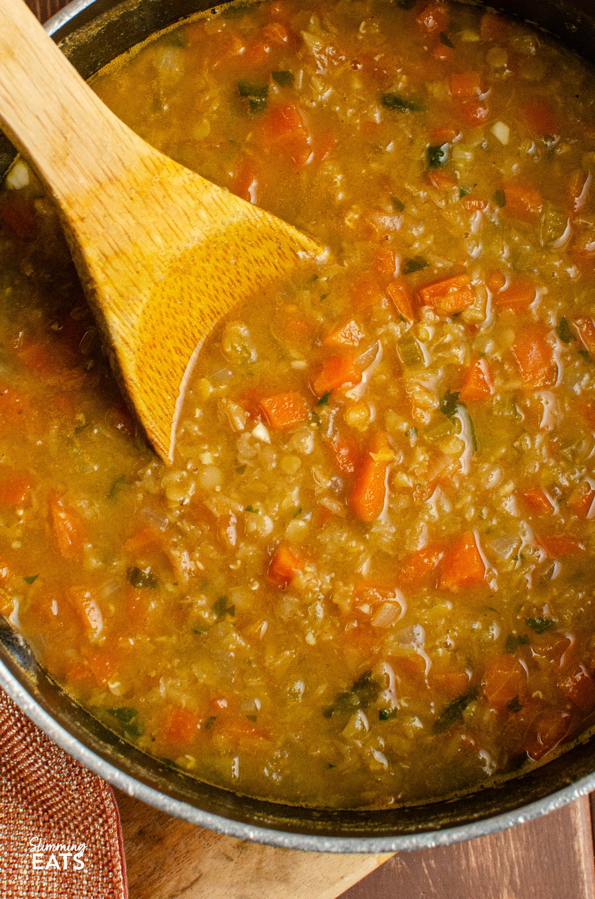 Spicy carrot and lentil soup in a saucepan with a wooden spoon placed inside the pot