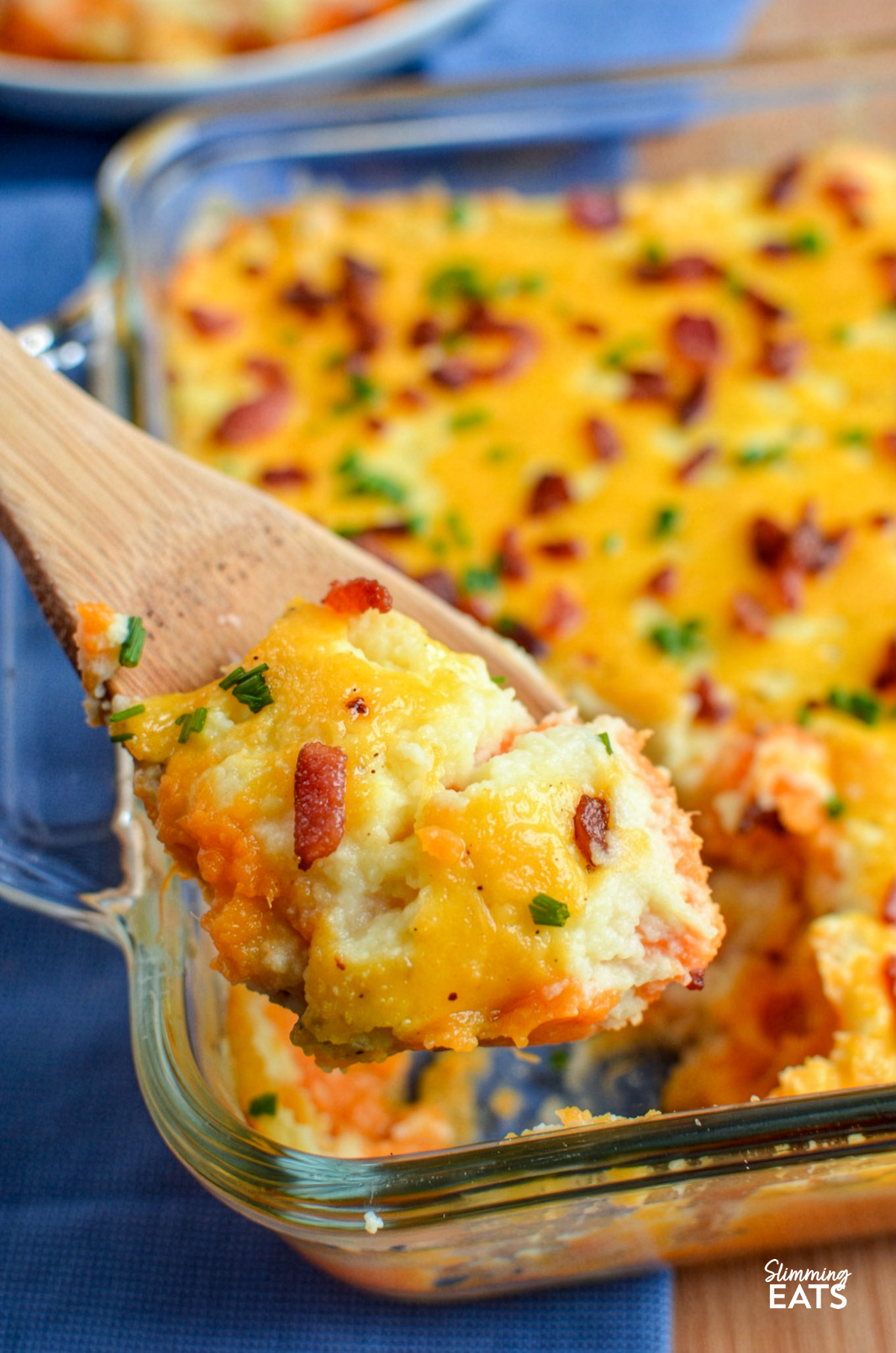 wooden spoon scooping up layered mashed potato casserole from a glass oven dish