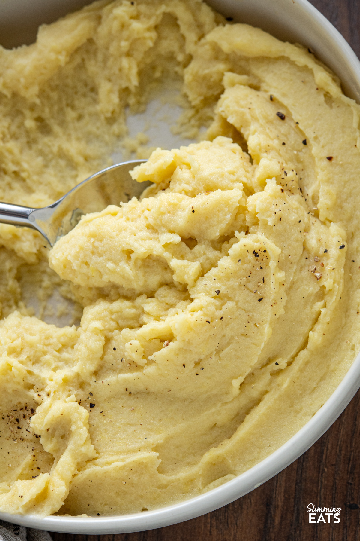 close up of lighter mashed potatoes in a white bowl with serving spoon