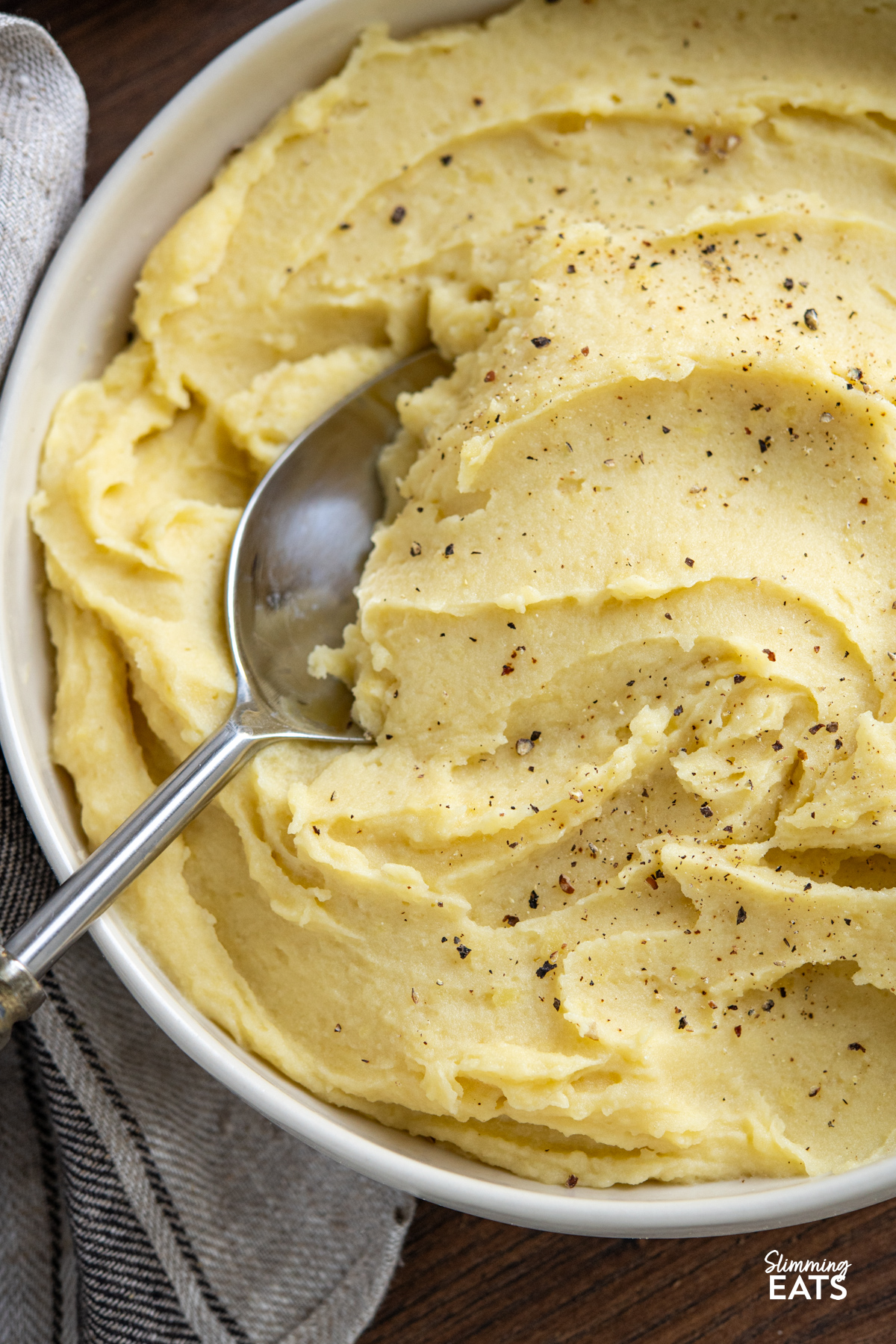 close up of lighter mashed potatoes in a white bowl with serving spoon