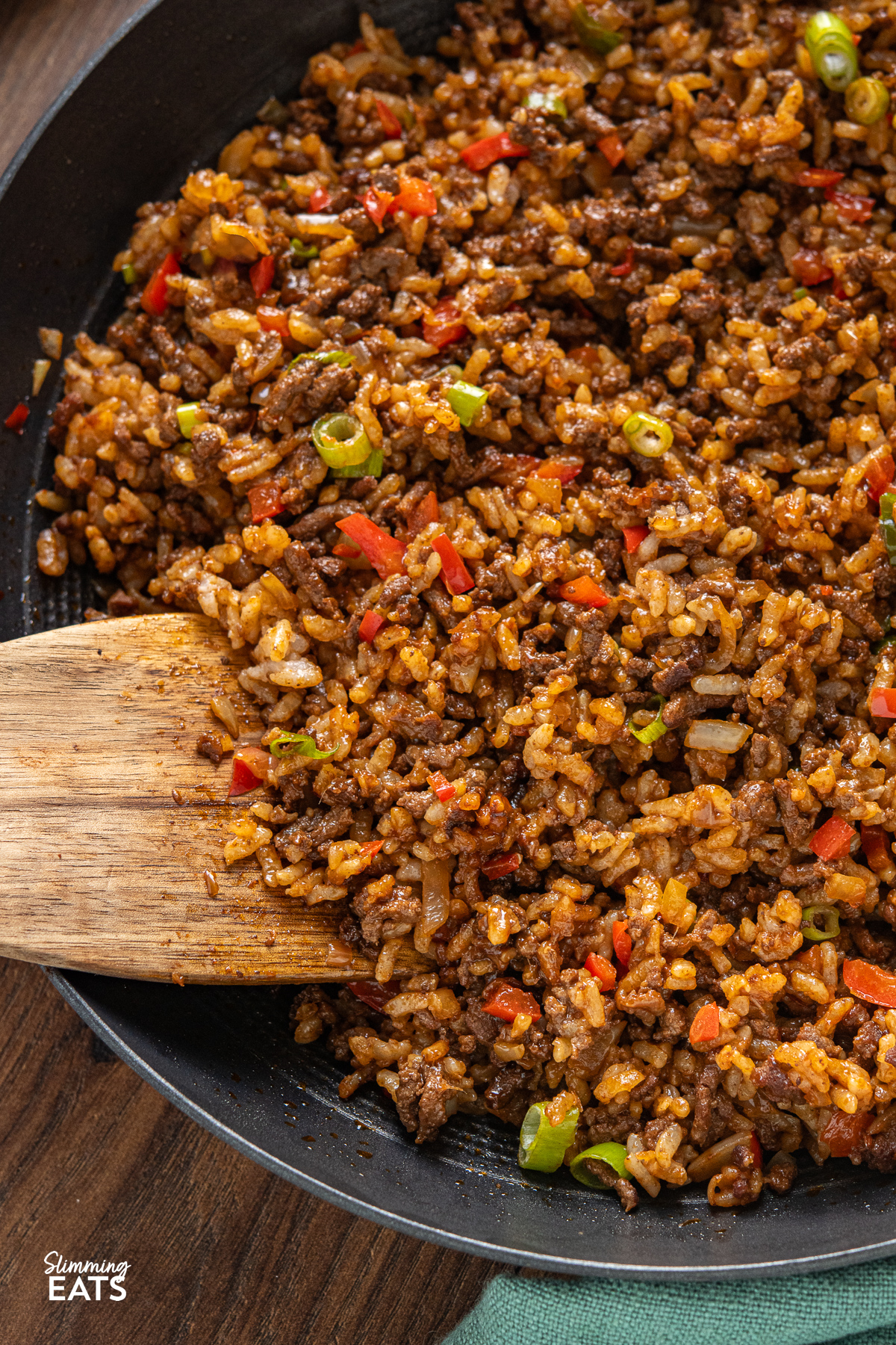 Discover the rich and savoury world of Indonesian cuisine with this tantalizing Nasi Goreng, a flavorful fried rice delight featuring beef mince, enhanced by a sweet and umami-packed soy sauce with a hint of spice. close up of Beef Nasi Goreng in a black frying pan with wooden spatula