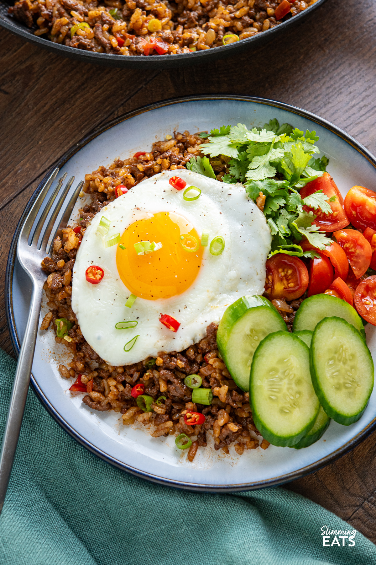 Served up nasi goreng topped with fried egg and served with tomatoes and cucumber in a pale blue bowl with navy rim.