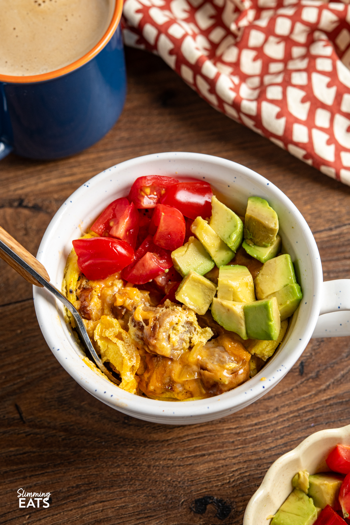 Need a quick breakfast that still feels filling? This Breakfast in a Mug is perfect for those mornings when you want something warm and satisfying, without spending ages in the kitchen. Breakfast in a Mug topped with tomatoes and avocado and blue mug with coffee and brown and cream towel above.