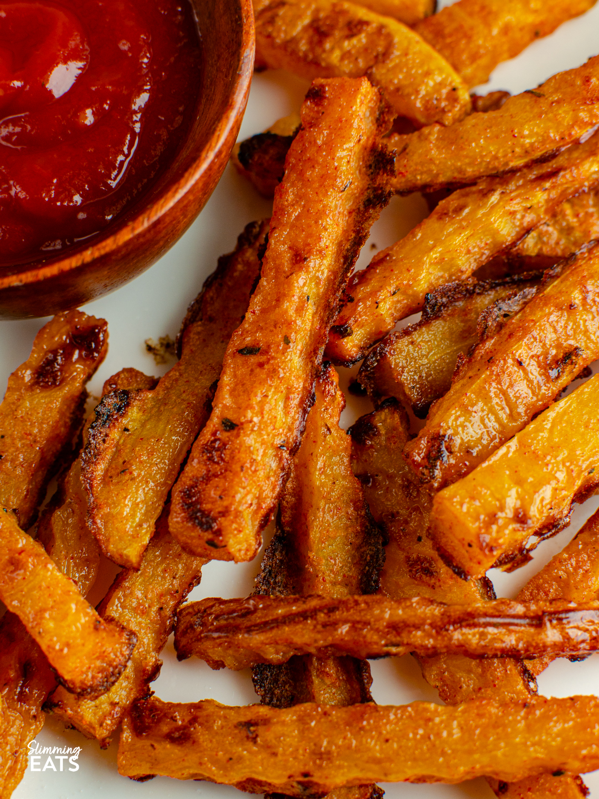 close up of cooked butternut squash fries with ketchup in a small wooden bowl