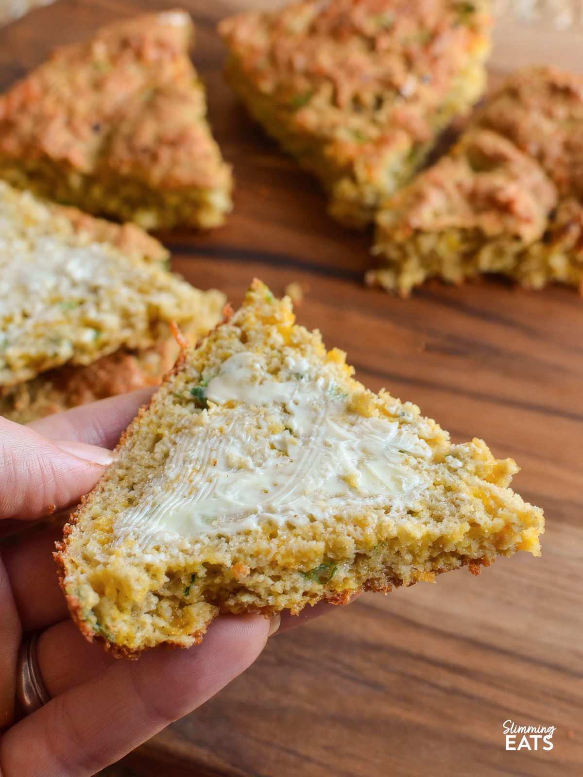 one slice of  buttered slices of Cheddar Spring Onion Oat Bread being picked up from a wooden board with hand. 