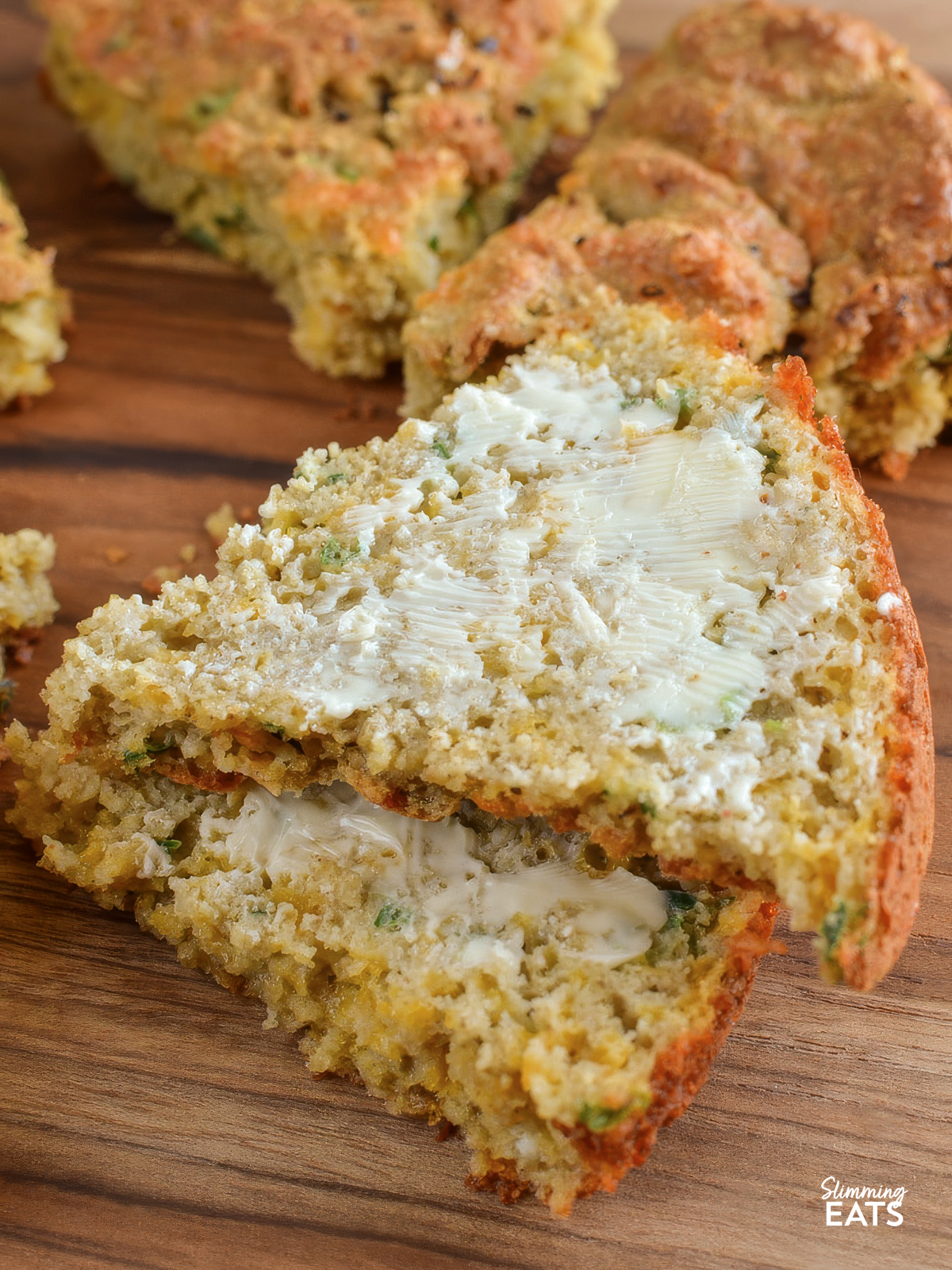 two buttered slices of Cheddar Spring Onion Oat Bread sliced on a wooden board