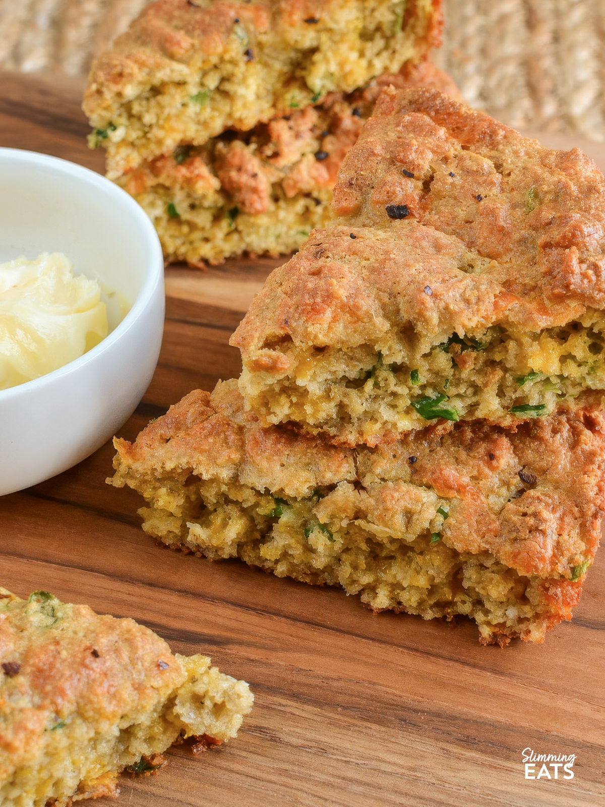 round Cheddar Spring Onion Oat Bread sliced into 6 slices on a board with a small bowl of butter