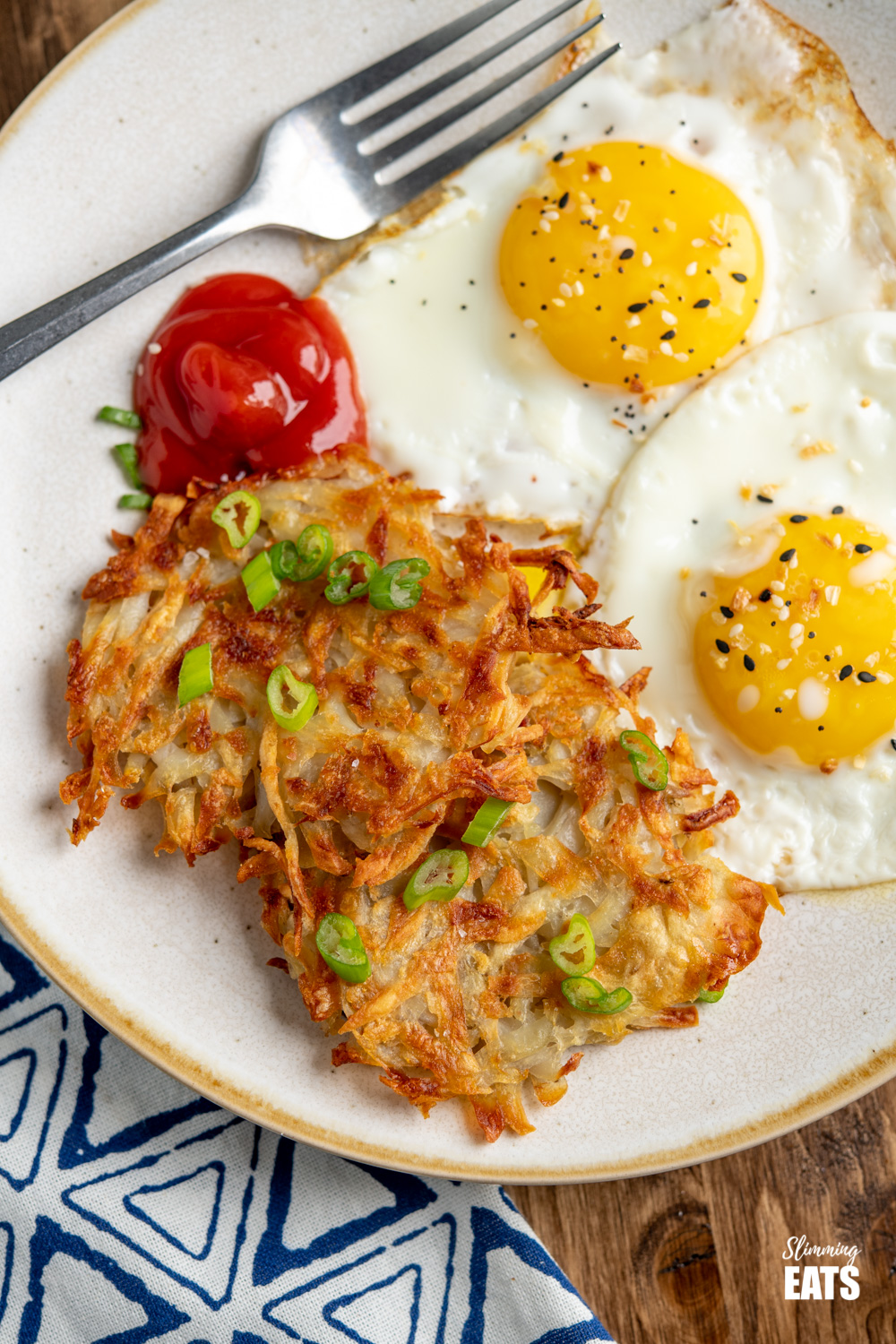 close up of Crispy Golden Hash Browns on plate sprinkled with spring onions and served with eggs and ketchup