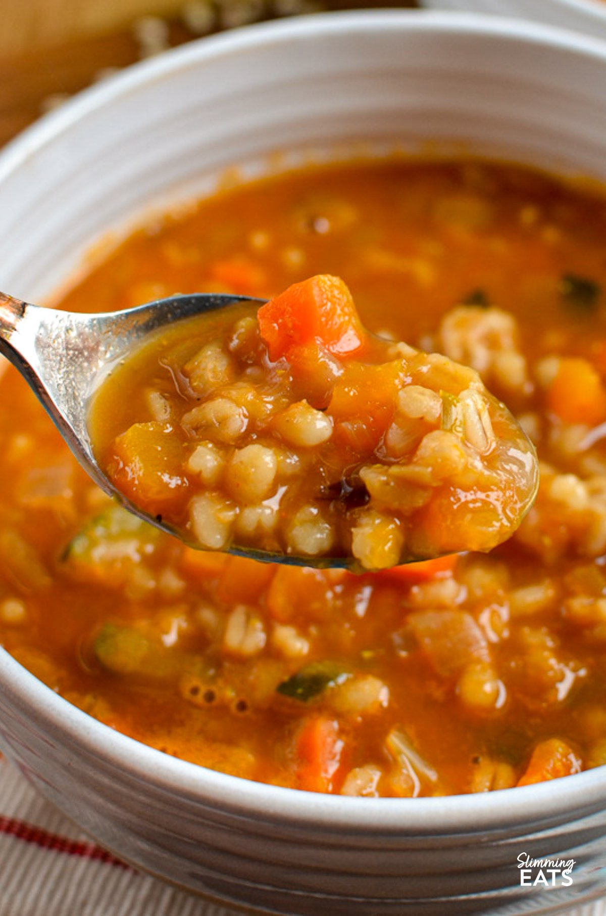 Vegetable Pearl Barley Soup in a white bowl, with a silver spoon scooping up some soup, showcasing the soup's hearty ingredients and texture.