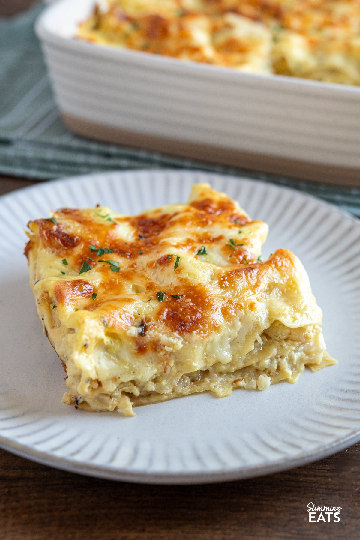 close up of Roasted cauliflower lasagne plated on a white grey plate  with the lasagne dish in the background.