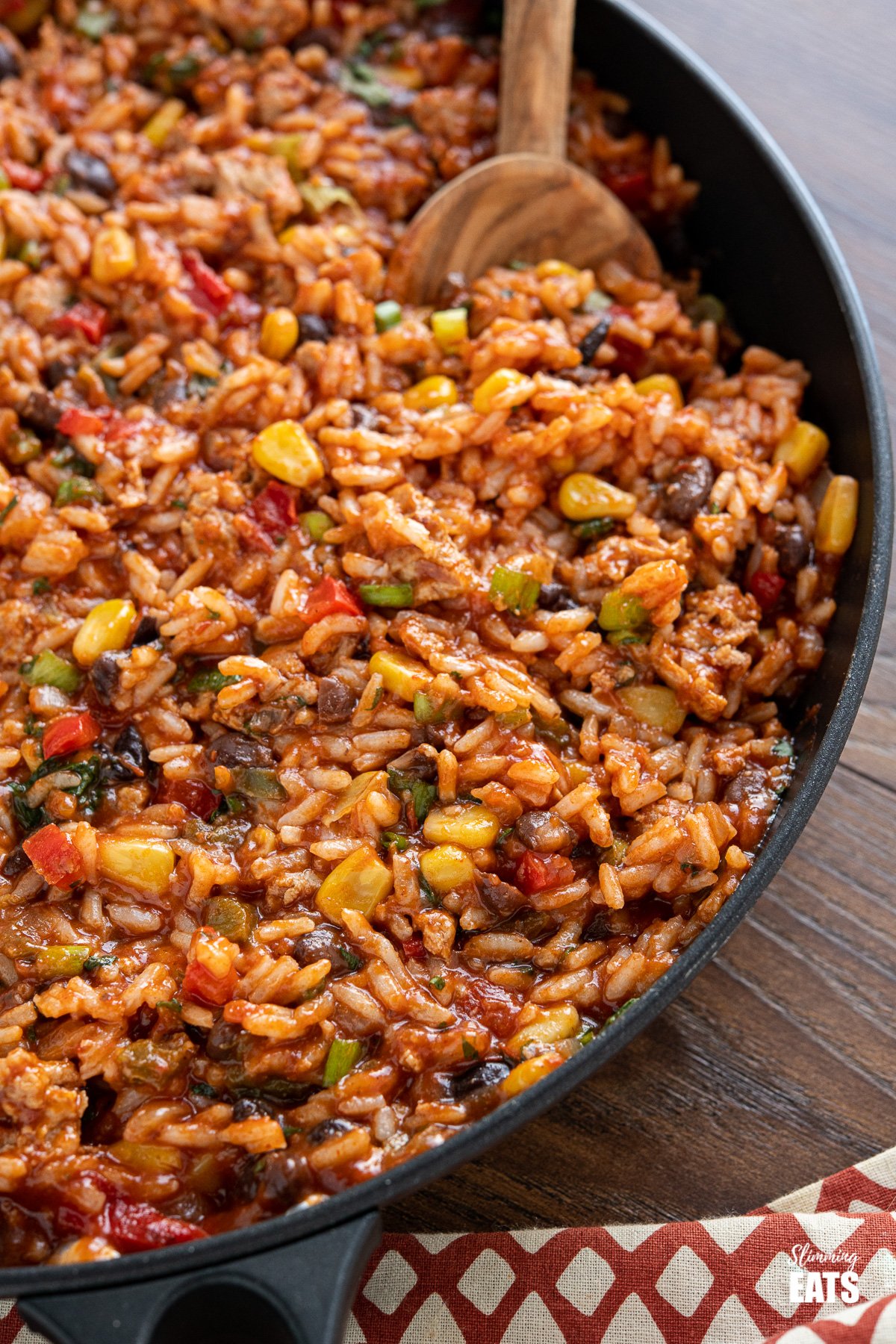 close up of turkey burrito rice in black frying pan with olive wood spoon