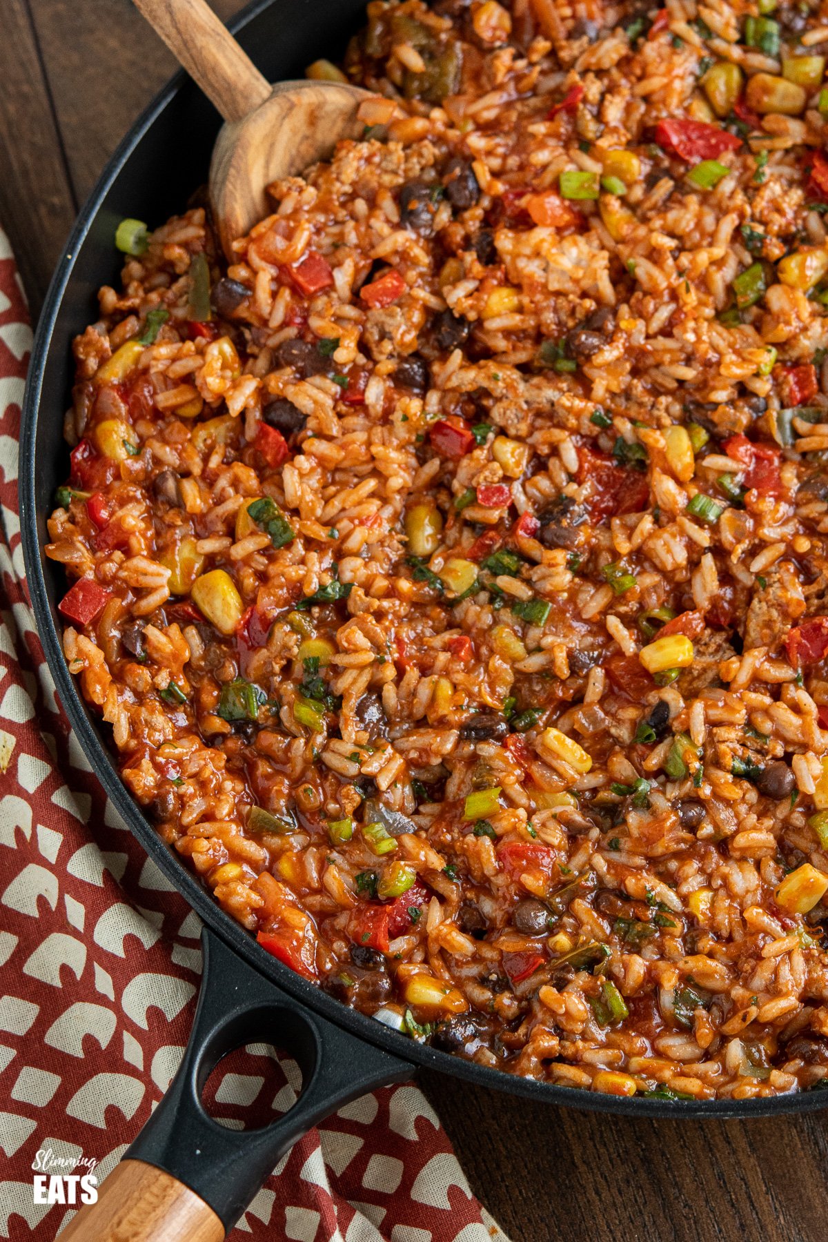 turkey burrito rice in black frying pan with olive wood spoon on wooden board