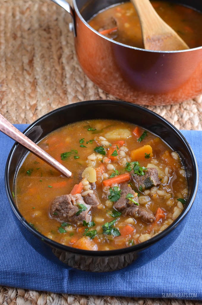 beef vegetable pearl barley soup in a black bowl with saucepan of soup in background