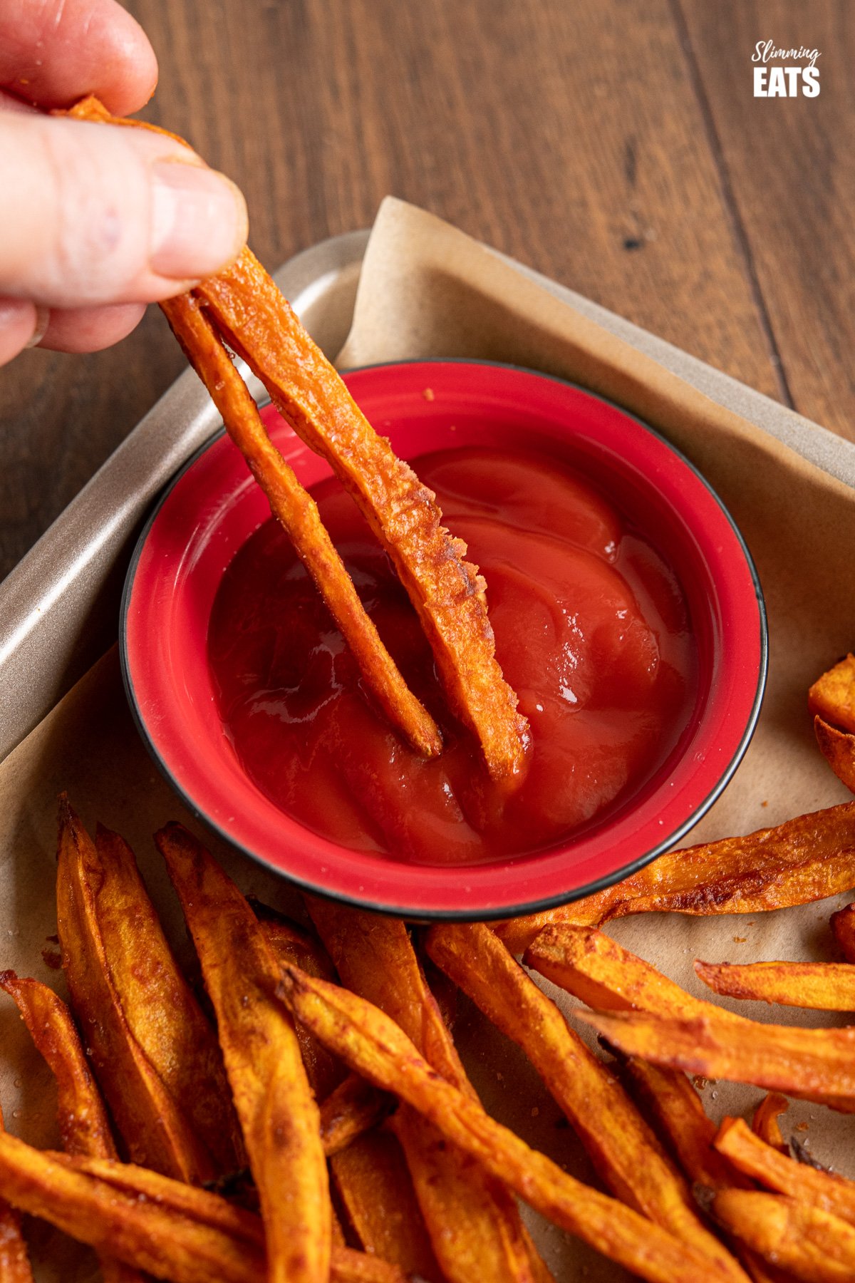 dipping Sweet Potato Fries from parchment lined tray into ketchup