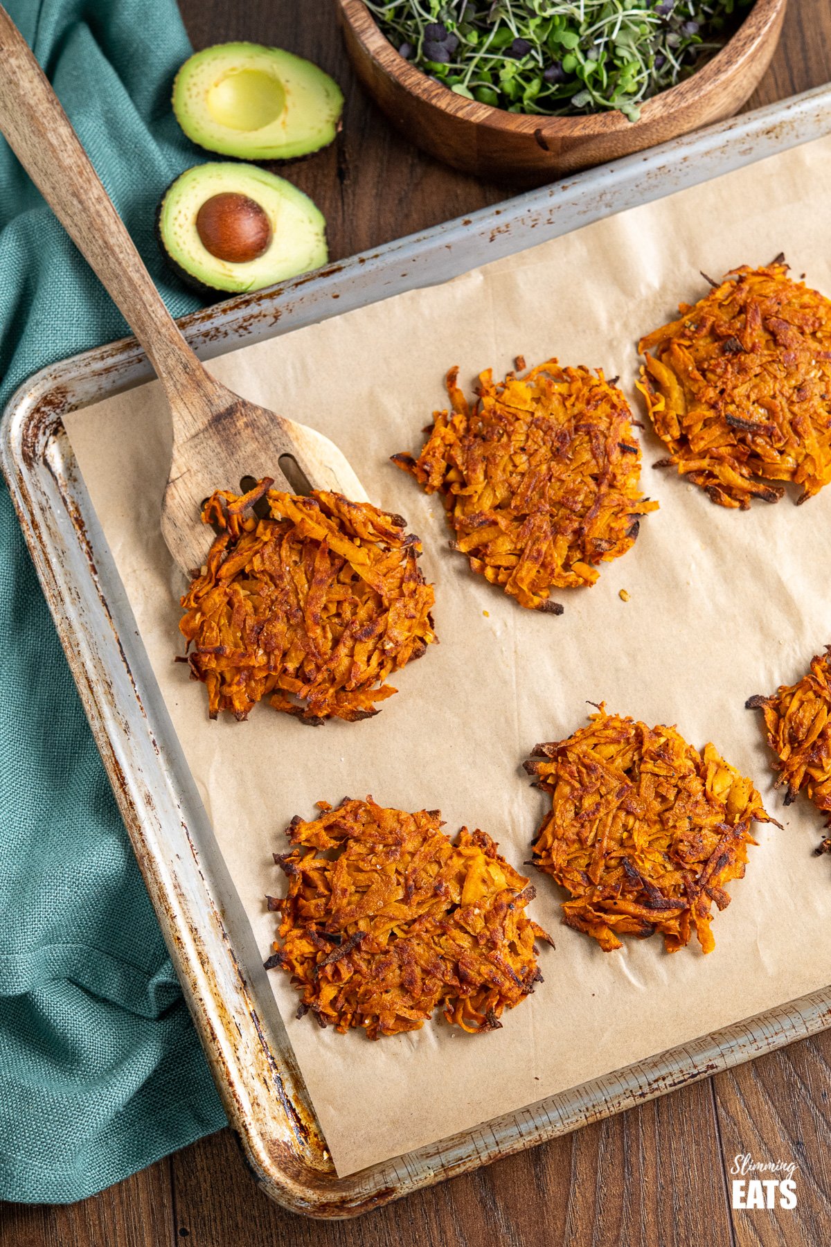 sweet potasto hash browns on a parchment lined tray with avocado sliced in half and microgreens in the background