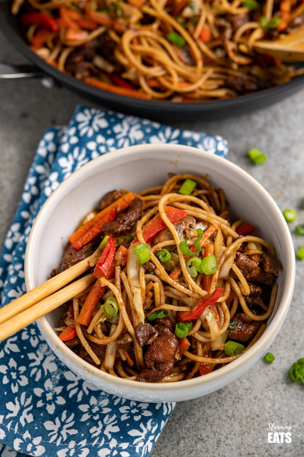 chicken with noodles and vegetables in a white bowl with chopsticks