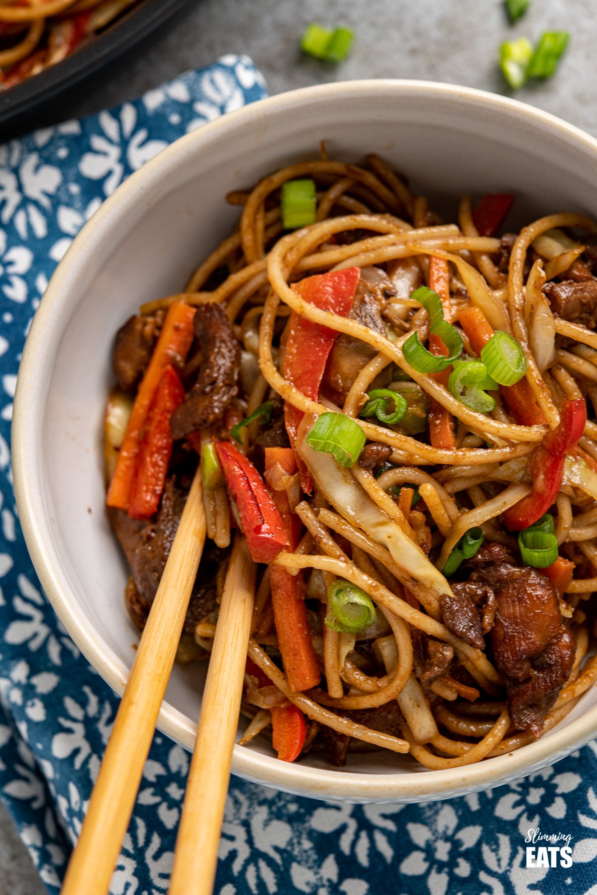 close up of chicken with noodles and vegetables in a white bowl with chopsticks