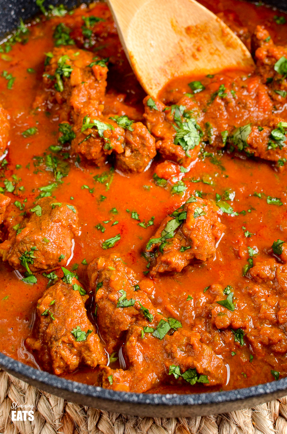 close up of Bombay Lamb Curry in black skillet with wooden spoon. 