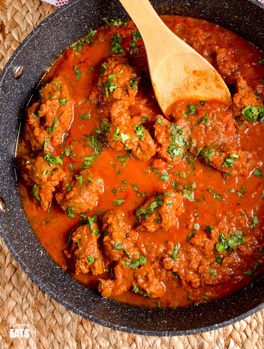 Bombay Lamb Curry in black skillet with wooden spoon. 