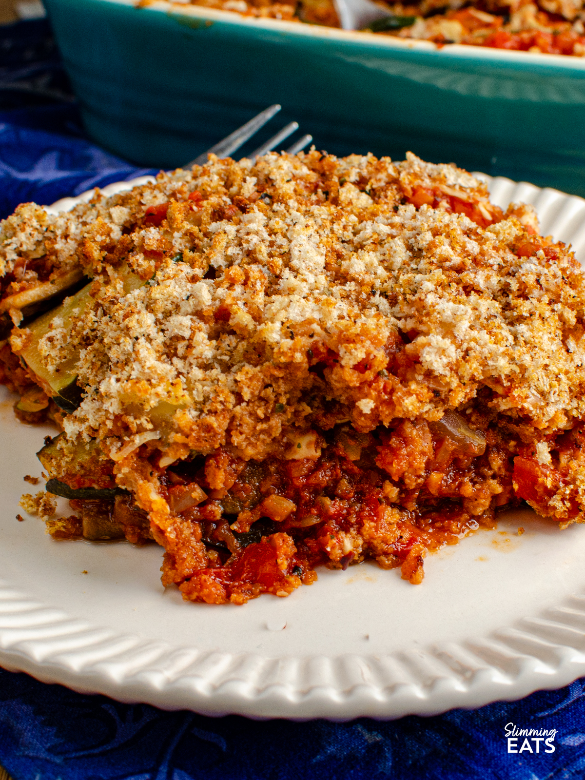 serving of Roasted Vegetable Gratin on a light cream plate with fork, baking dish in background
