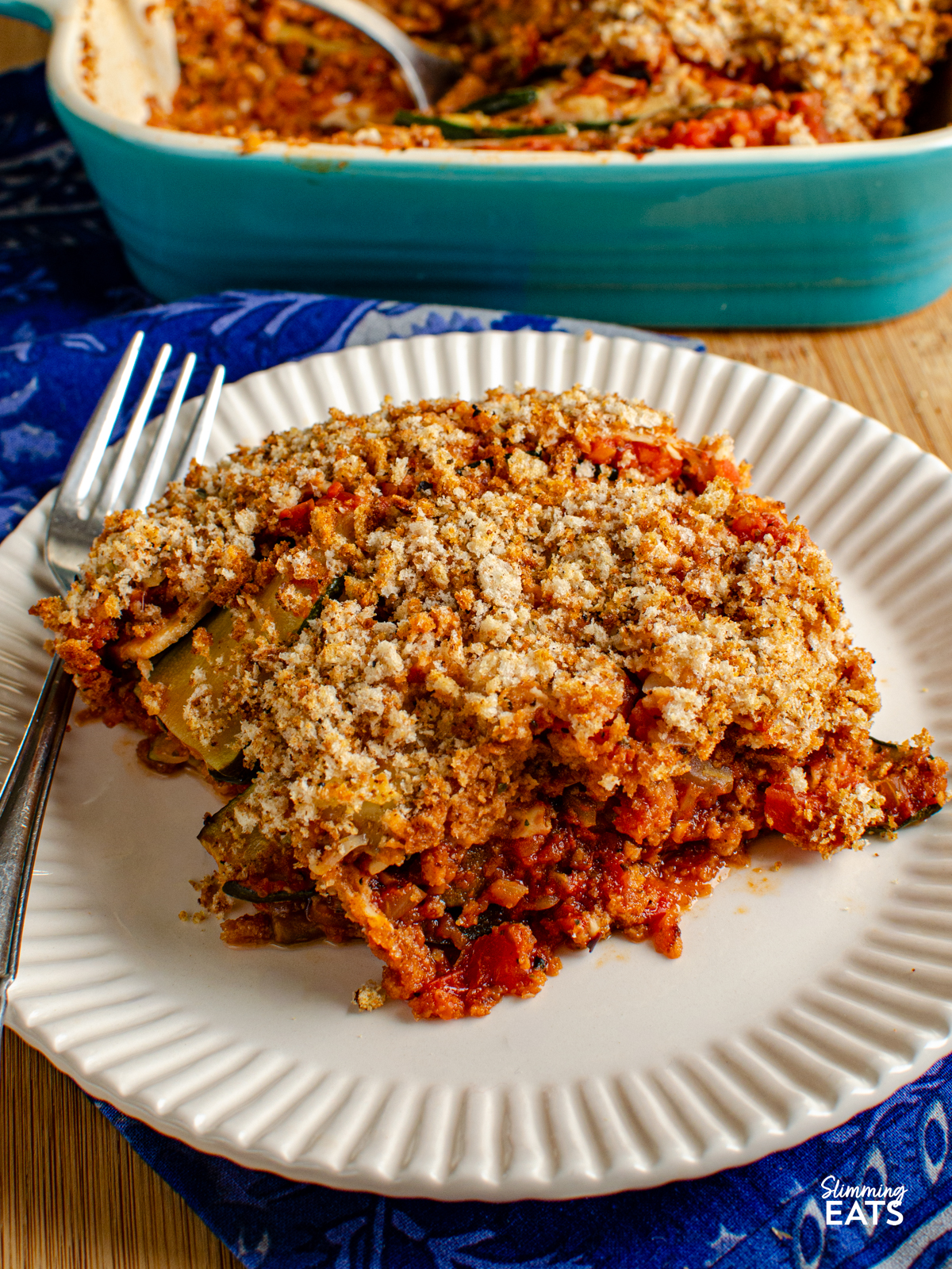 serving of Roasted Vegetable Gratin on a light cream plate with fork, baking dish in background