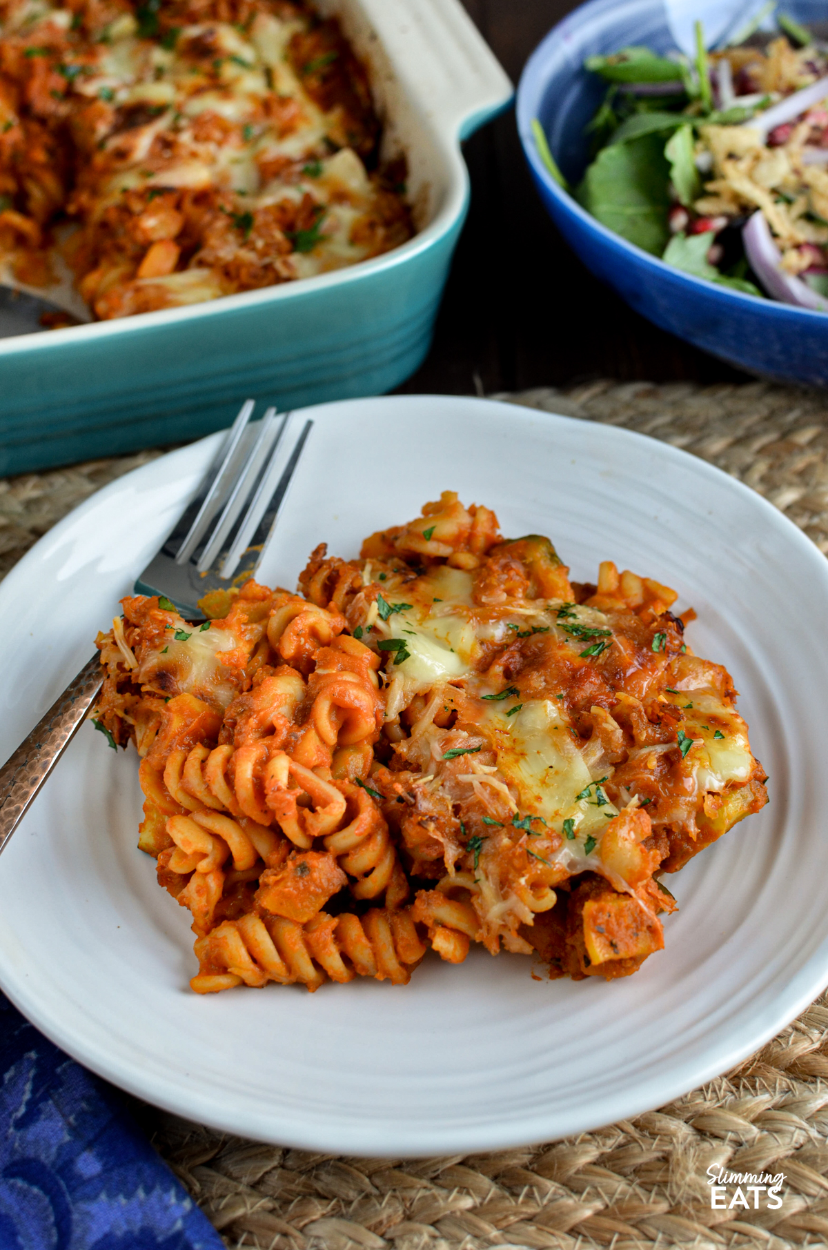 Roasted Butternut Squash Zucchini Pasta Bake - a simple comforting pasta bake with roasted butternut squash, zucchini and pasta baked in a tomato sauce with a delicious cheesy topping. It is an easy family friendly dinner that comes together with very little fuss and is perfect for busy evenings. Roasted Butternut Squash Zucchini Pasta Bake on a white plate with fork, ceramic dish with pasta bake in background with bowl of salad.