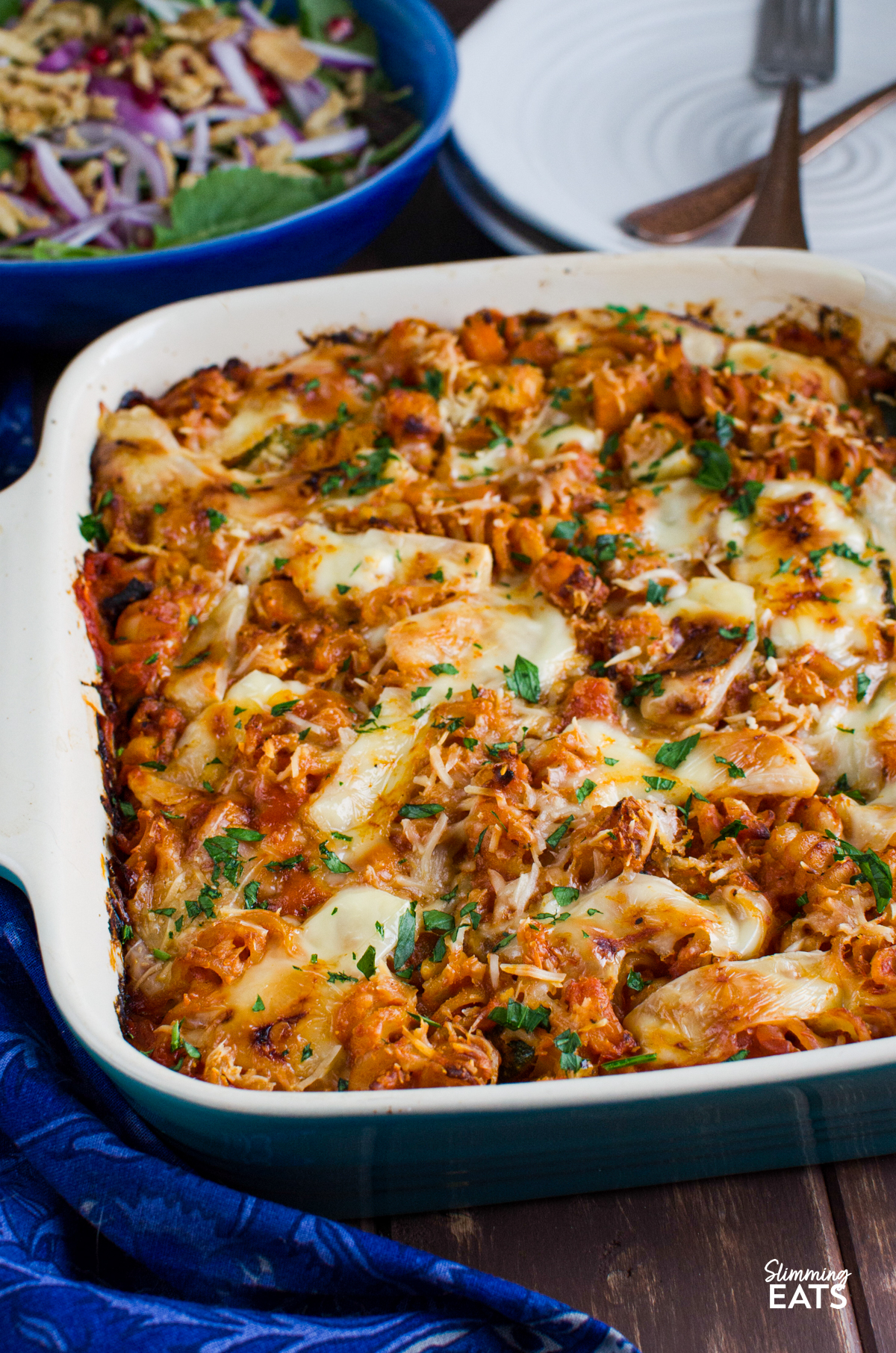 Roasted Butternut Squash Zucchini Pasta Bake - a simple comforting pasta bake with roasted butternut squash, zucchini and pasta baked in a tomato sauce with a delicious cheesy topping. It is an easy family friendly dinner that comes together with very little fuss and is perfect for busy evenings. Roasted Butternut Squash Zucchini Pasta Bake in ceramic oven dish with bowl of salad and white plates with gold forks on top in background