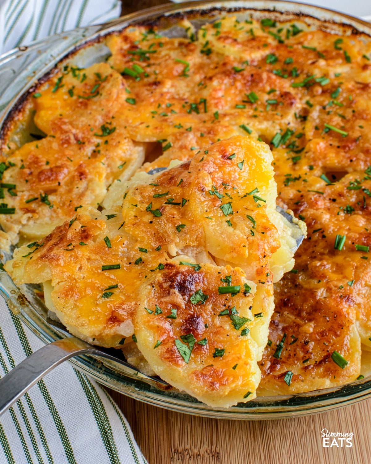 slice of scalloped potatoes baked and out of oven being taken out of a glass round dish