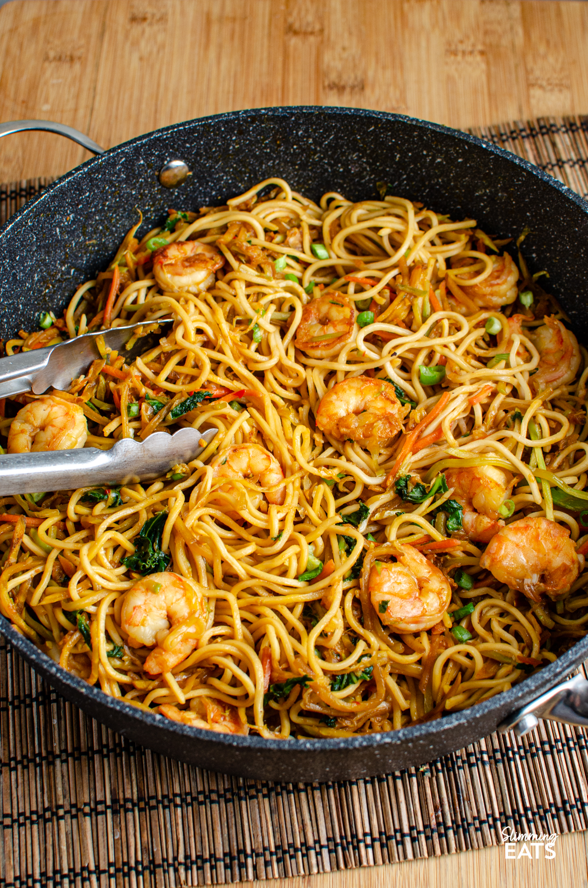 Sweet Chilli Prawn Noodles - an easy dinner that is packed with flavour and ready in less than 30 minutes. Juicy prawns, crisp vegetables and noodles are tossed together in a sweet, chilli sauce with just the right amount of heat for a quick meal that the whole family can enjoy. Sweet Chilli Prawn Noodles in a non stick frying pan with metal tongs