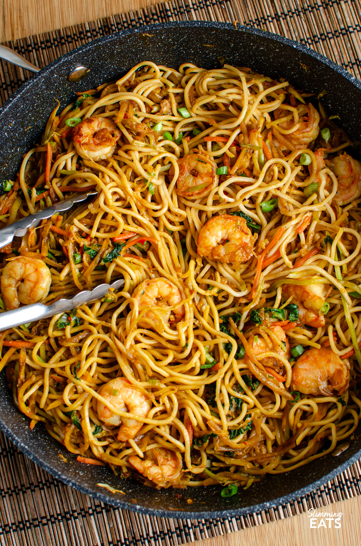Sweet Chilli Prawn Noodles - an easy dinner that is packed with flavour and ready in less than 30 minutes. Juicy prawns, crisp vegetables and noodles are tossed together in a sweet, chilli sauce with just the right amount of heat for a quick meal that the whole family can enjoy. Sweet Chilli Prawn Noodles in a non stick frying pan with metal tongs