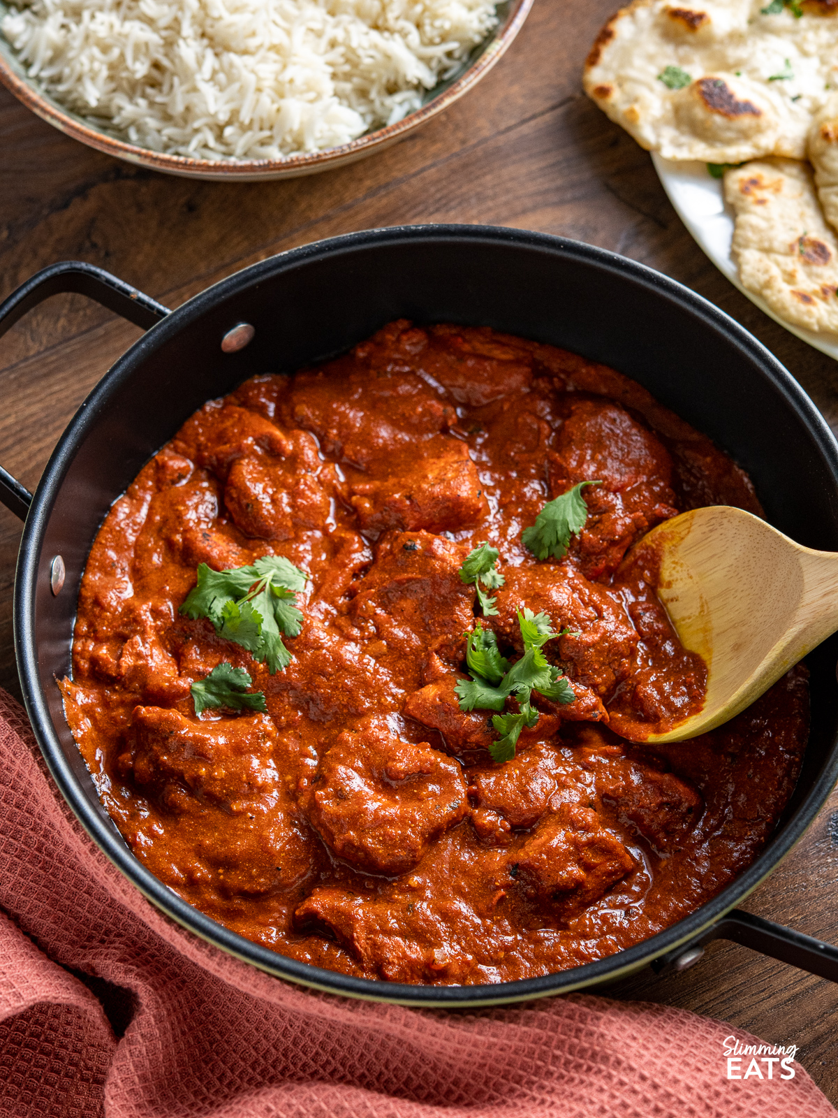 Chicken Tikka Masala in black pan with two handles and bowl of rice and naan in background