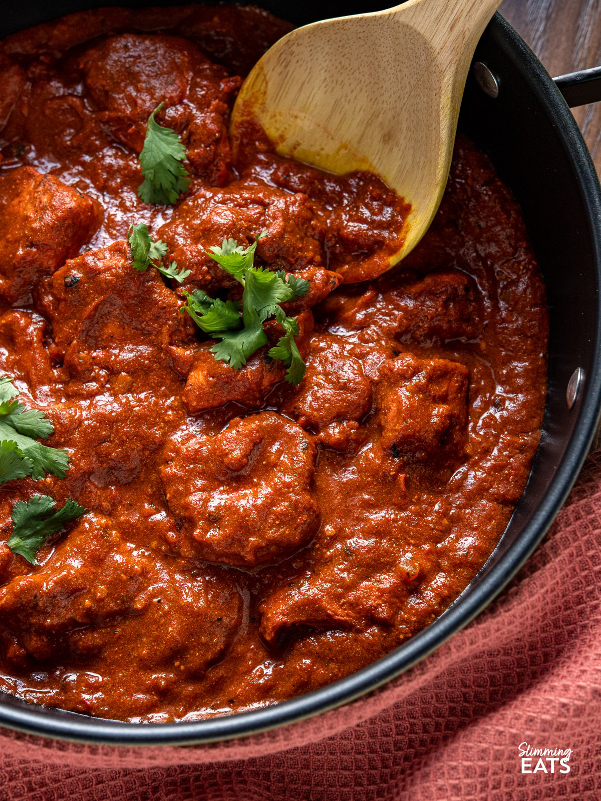 close up of Lighter Chicken Tikka Masala in black pan with wooden spoon 