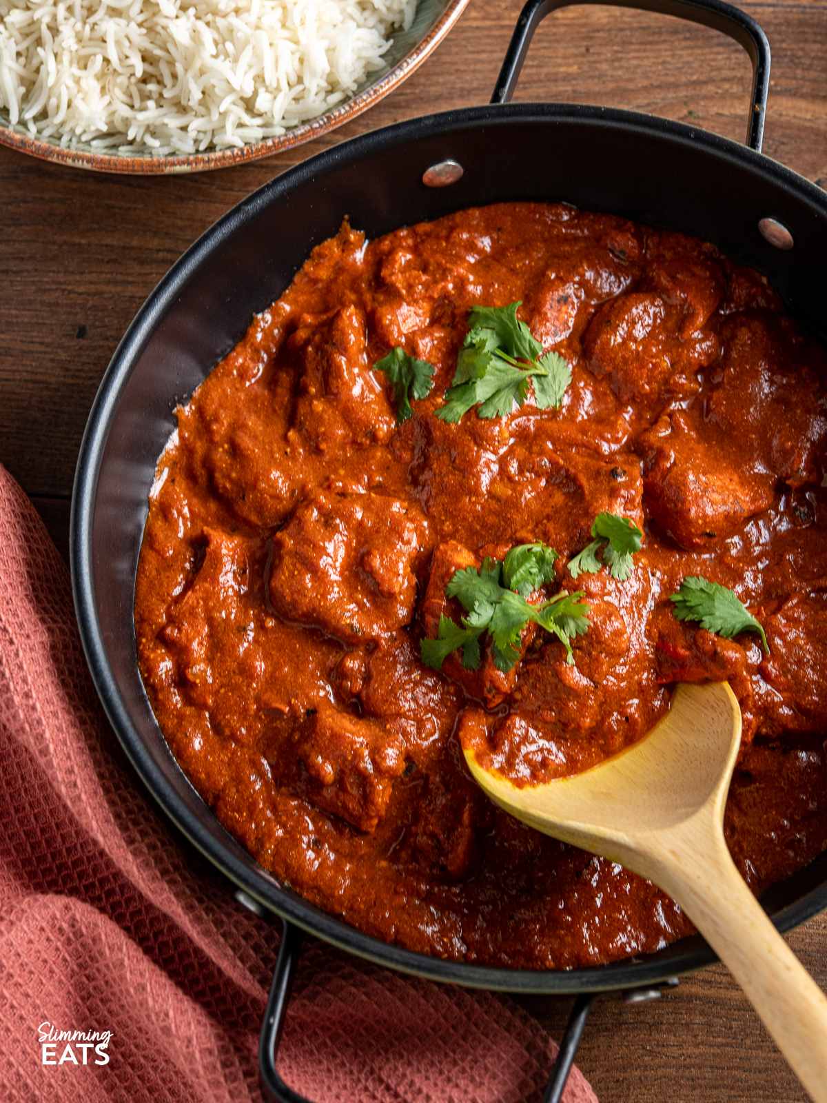 close up of Lighter Chicken Tikka Masala in black pan with wooden spoon 