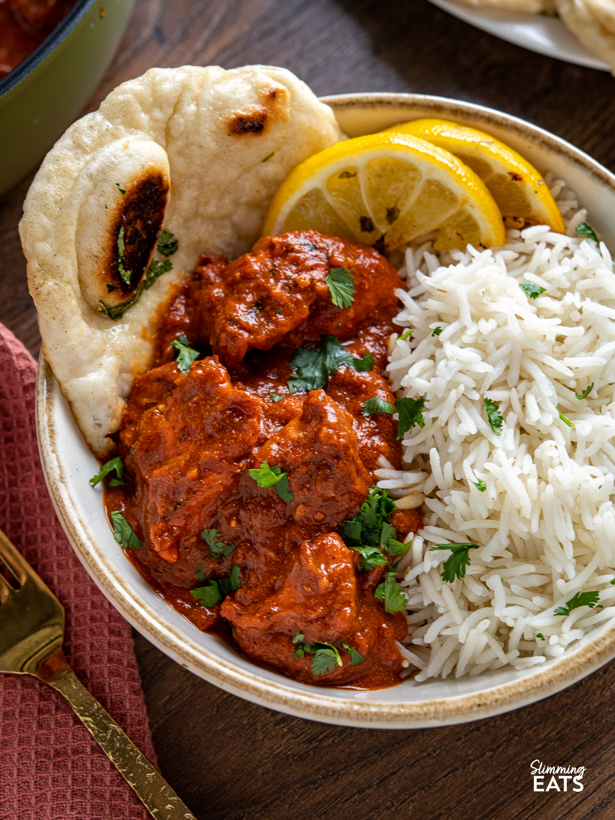 close up of Lighter Chicken Tikka Masala in white bowl with tan rim served with rice, naan and lemon slices