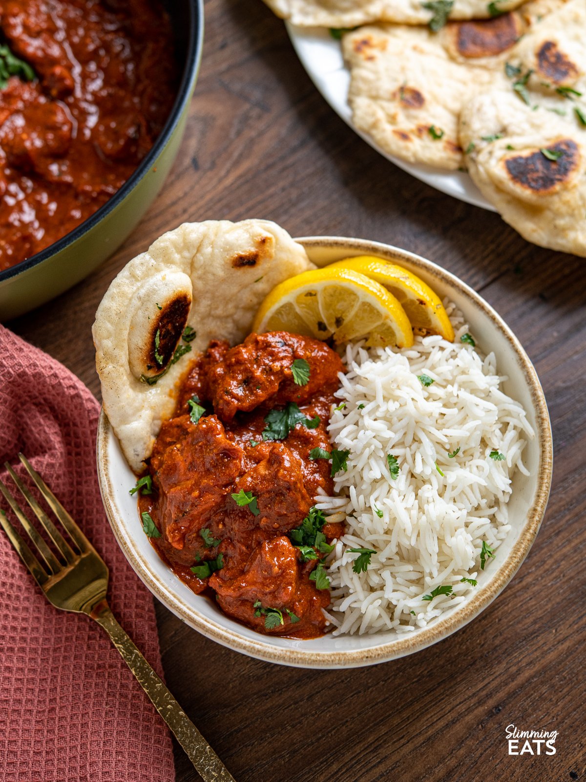 Lighter Chicken Tikka Masala in white bowl with tan rim served with rice, naan and lemon slices
