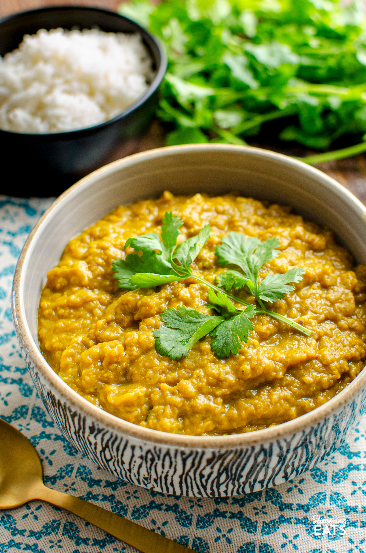 red lentil dhal in a bowl with black bowl of rice and fresh coriander in background