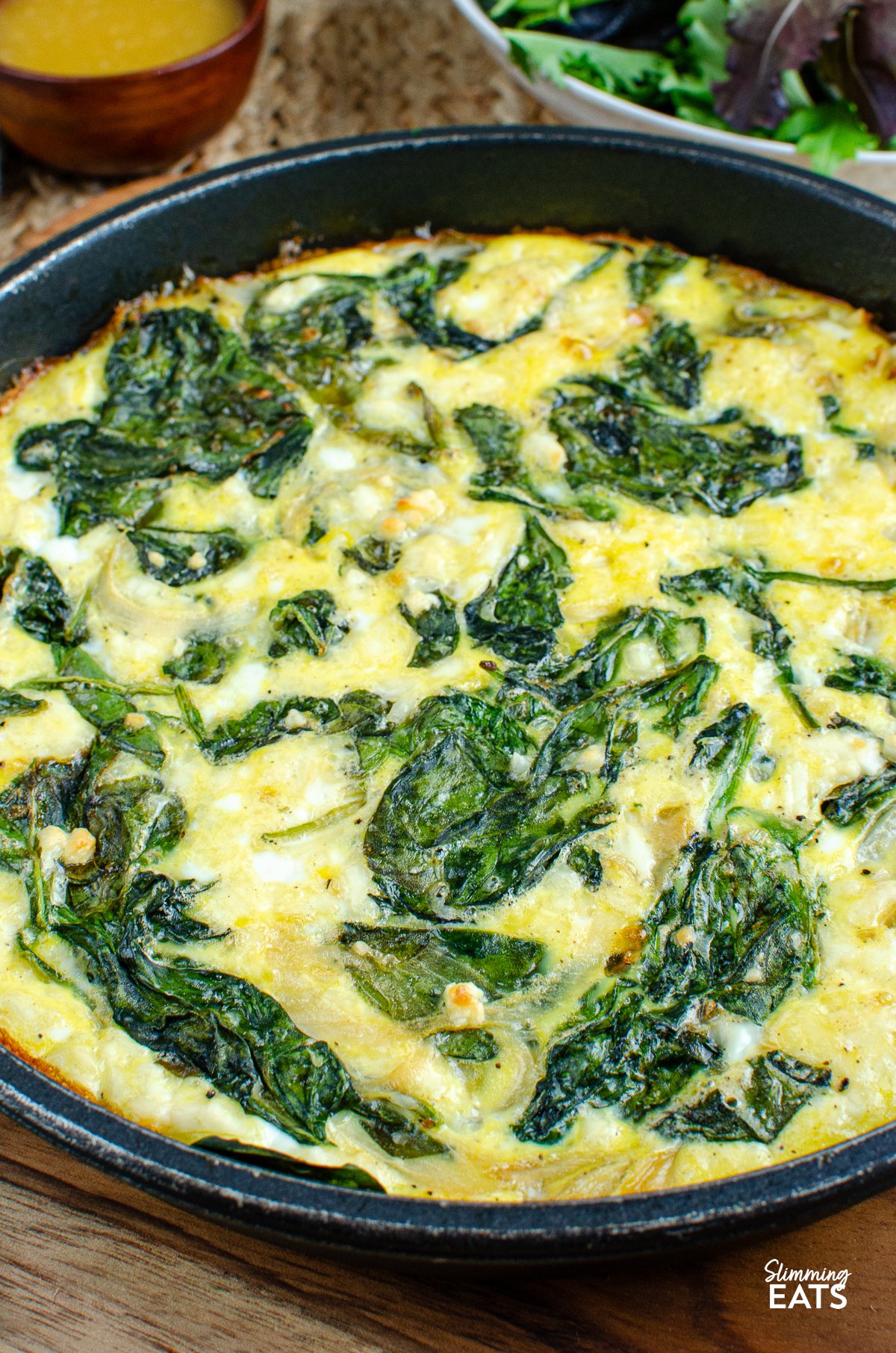 Spinach and Feta Frittata showcased in a skillet, accompanied by a bowl of fresh salad and vinaigrette in the background