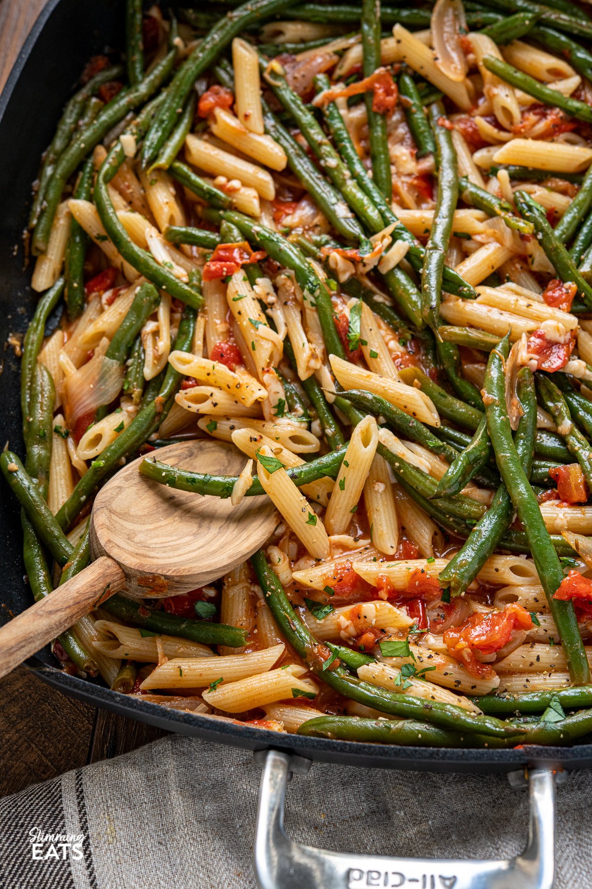 close up of Roasted Green Bean and Tomato Pasta in all clad square skillet with olive wood spoon