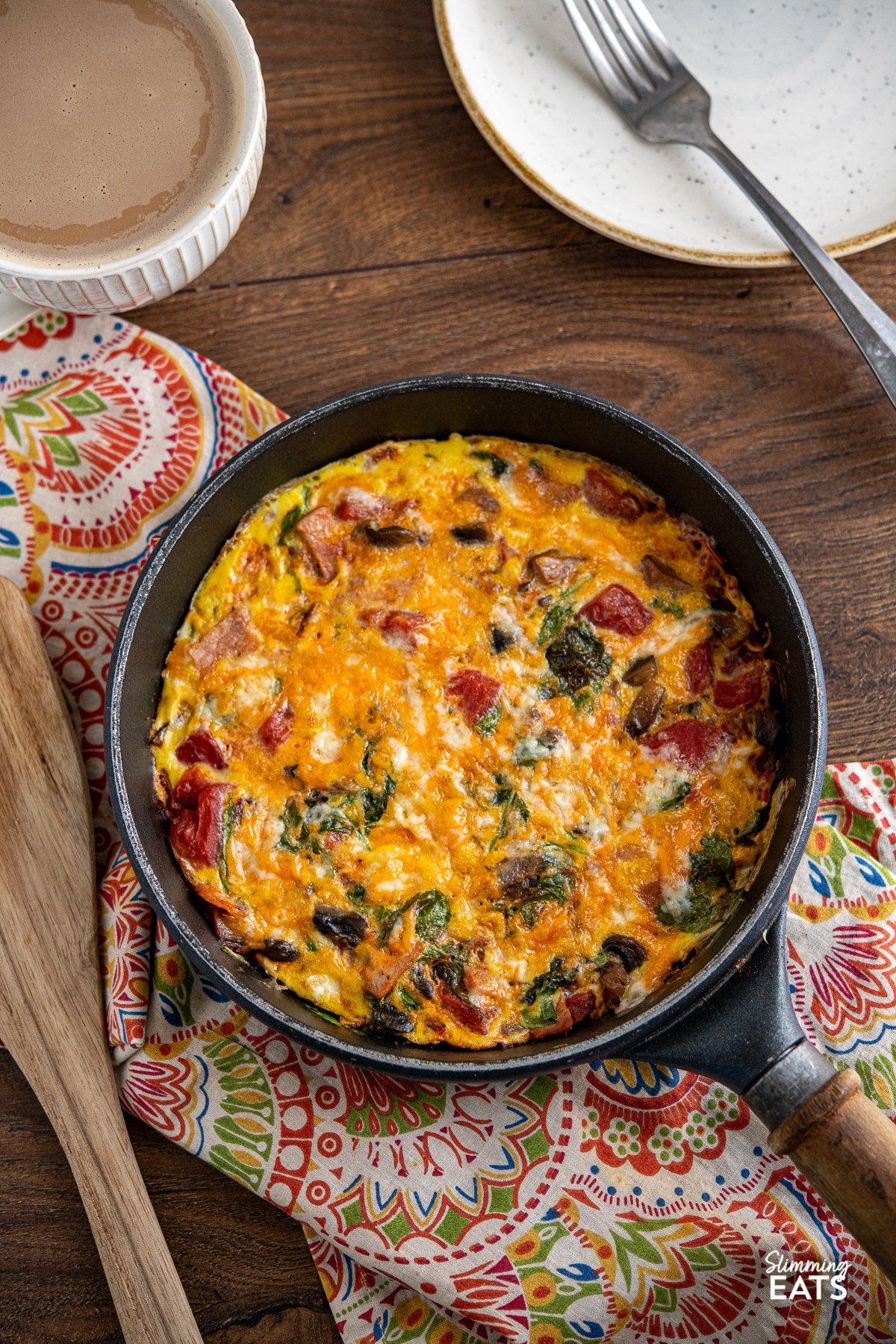 Speedy Breakfast Frittata in pan with wooden handle, plate with fork and cup of coffee in background