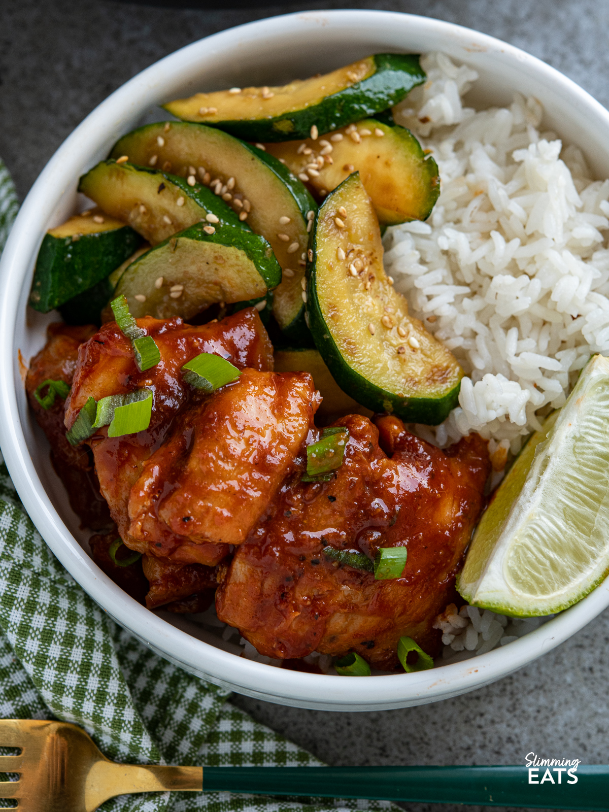 close up of sriracha chicken in a white bowl with sauteed zucchini and jasmine rice with a lime wedge.