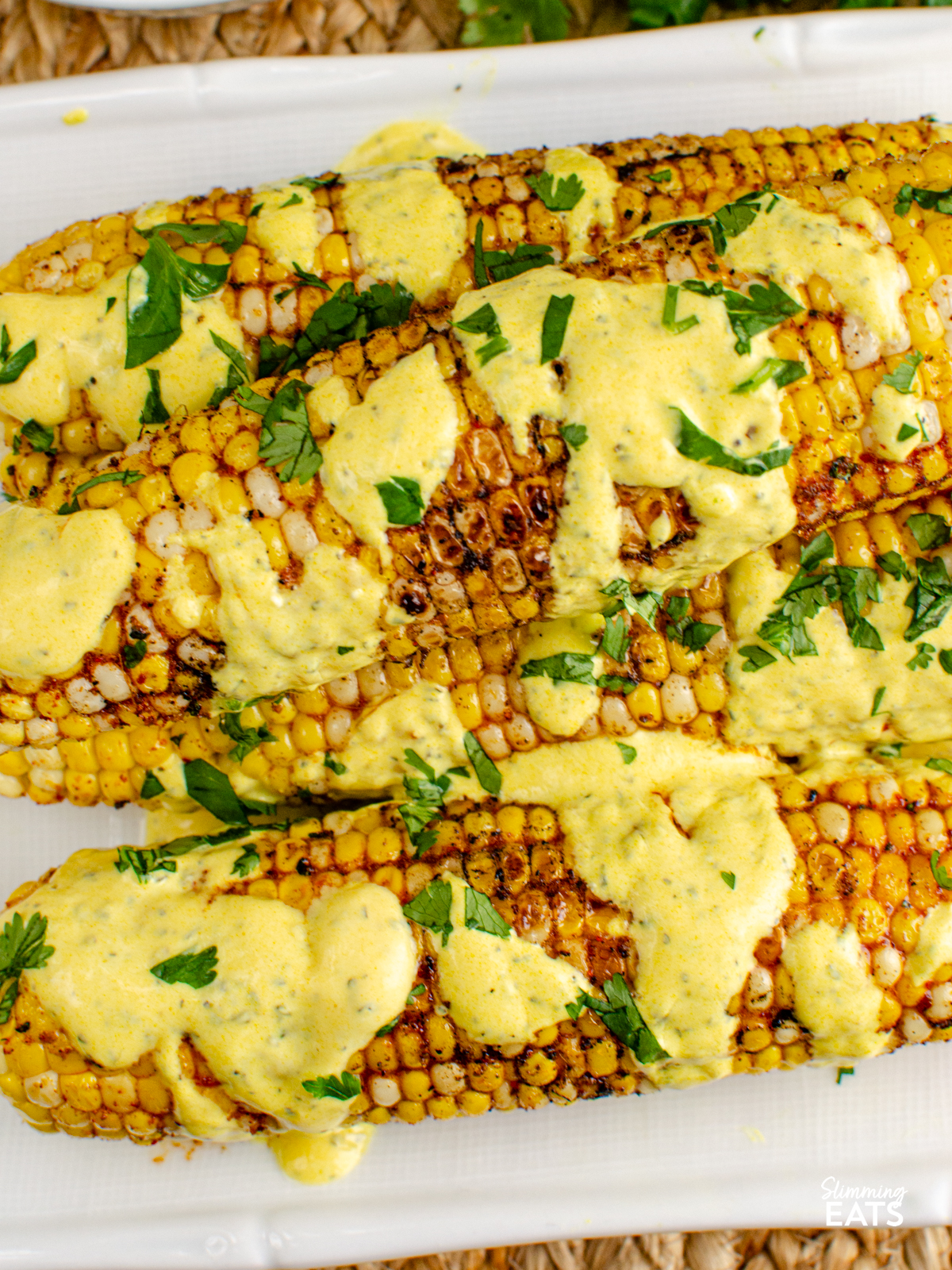 Indian Spiced Corn on the Cob on a white plate drizzled with mint yoghurt